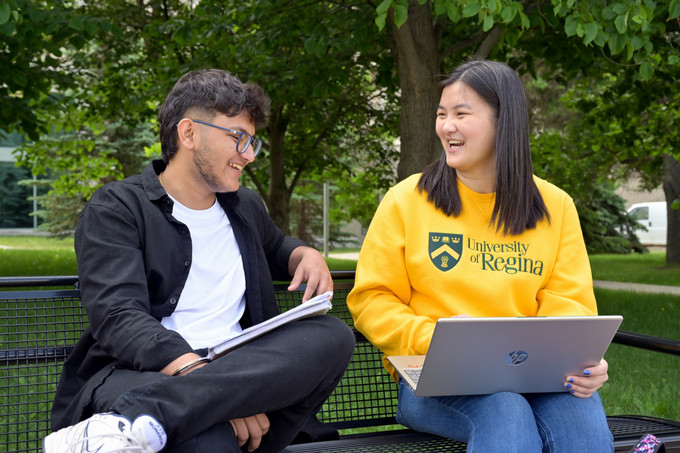 Two people sitting on a bench and looking at a laptop