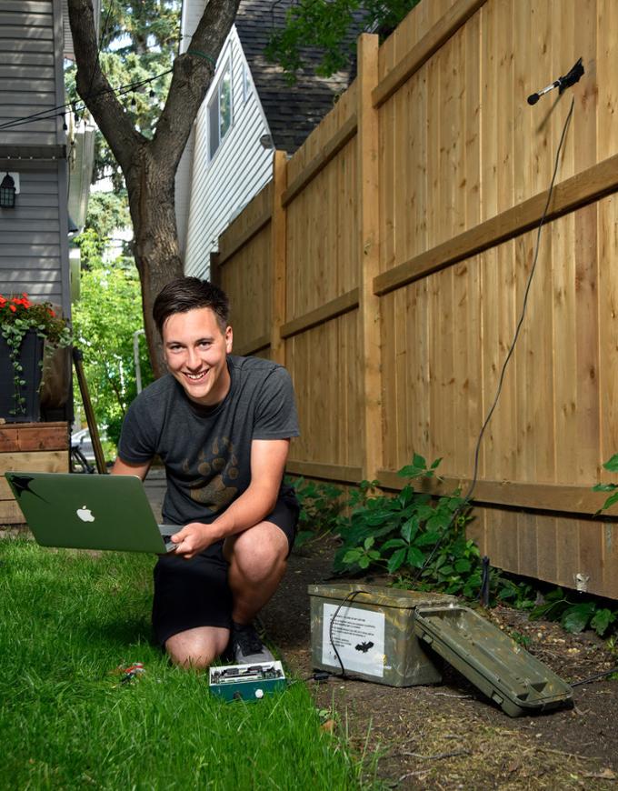 student outdoors by fence doing research on laptop