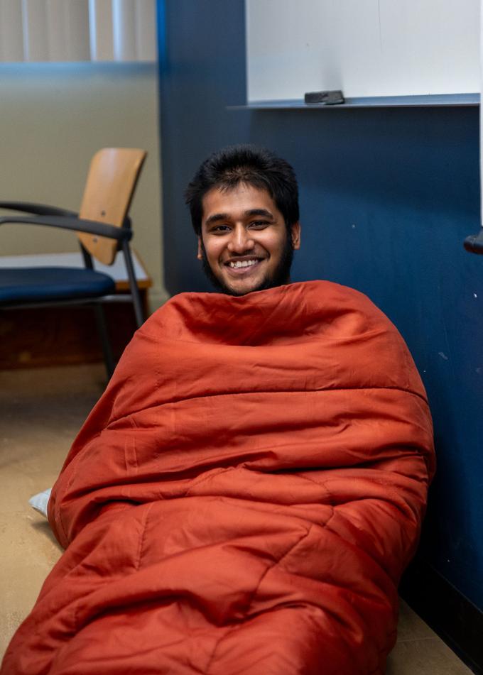 A participant is sitting on the floor of his team's room wrapped in a blanket. 