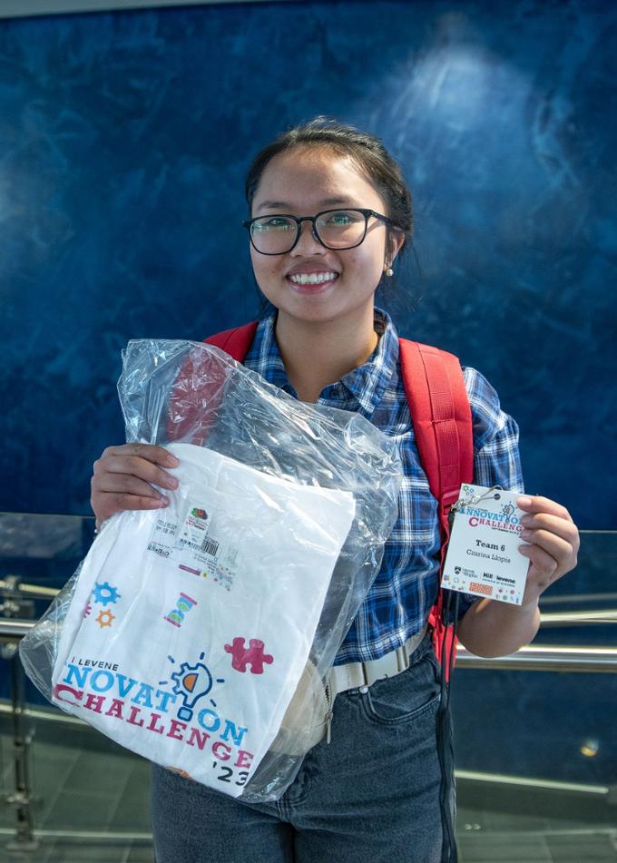 A student holds up her Innovation Challenge t-shirt and name tag.