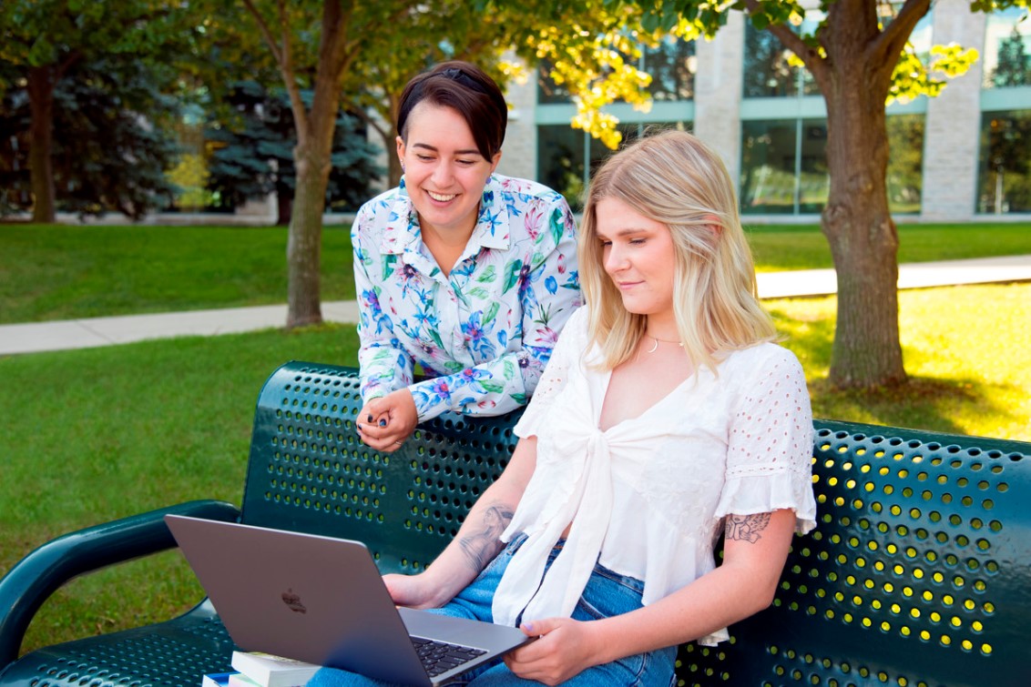 Two girls smiling at a laptop outside