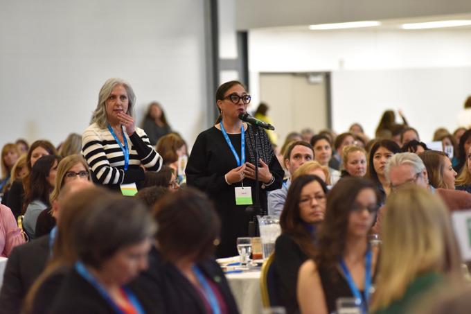 Two women waiting a microphone to ask a question at a conference.