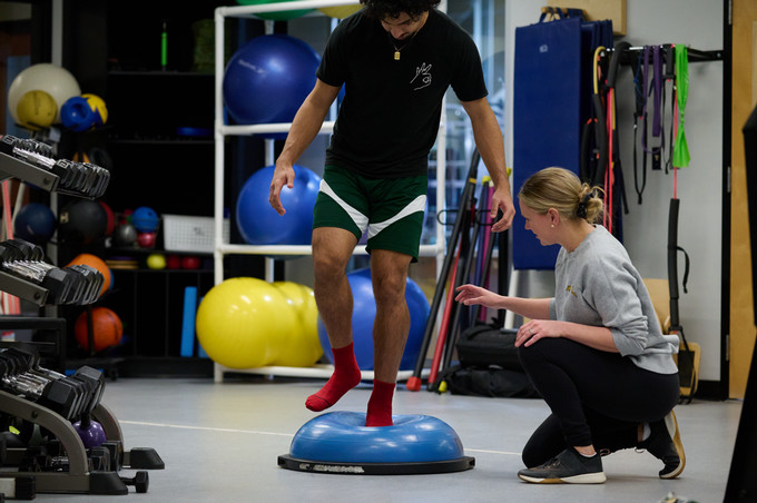 Physiotherapist assessing balance of patient by observing the patient balance on a bosu ball with one leg