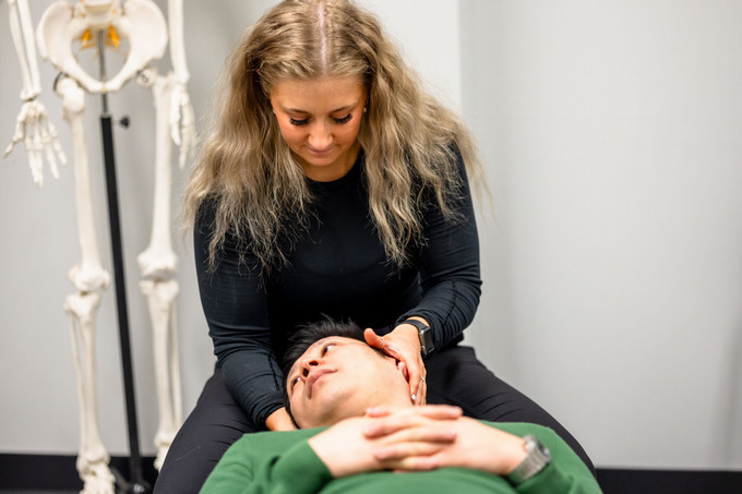 A chiropractor is conducting a neck and spine assessment on a patient who is laying down on a chiropractic bed