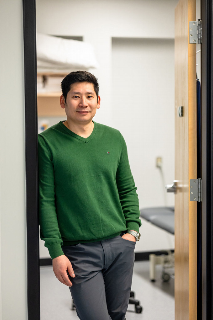 A headshot of a smiling physiotherapist, Mr. Khiem Nguuyen, leaning against the doorway of his office