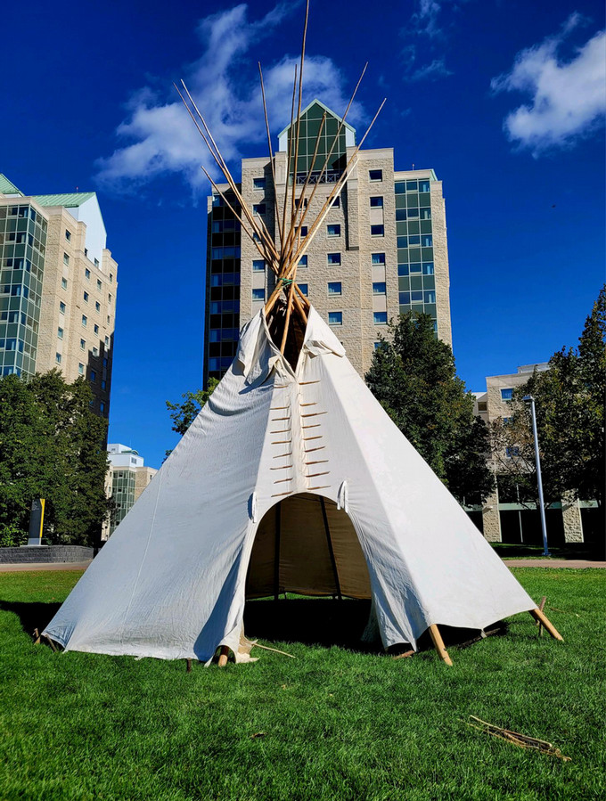 White tipi raised on the U of R Campus grounds on a bright sunny day.