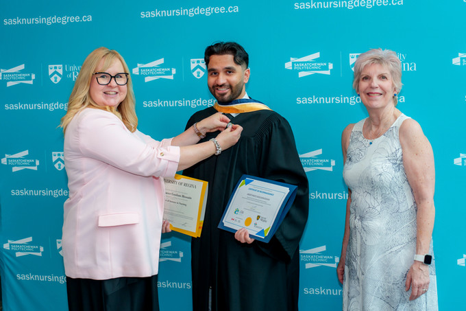 2 female nursing deans with male bilingual nurse graduate. One dean is placing pin his robe.