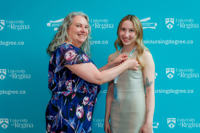 a female nursing graduate smiling at camera and her mom and placing the nursing pin on her