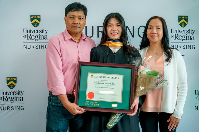 a female nursing graduate surrounded on each side by her mom and dad holding her diploma