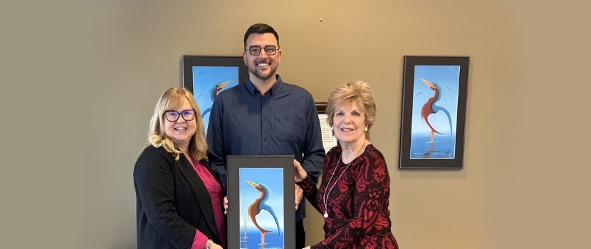 Nurse practitioner graduate holding a painting of a crane surrounding by the Deans of Nursing.