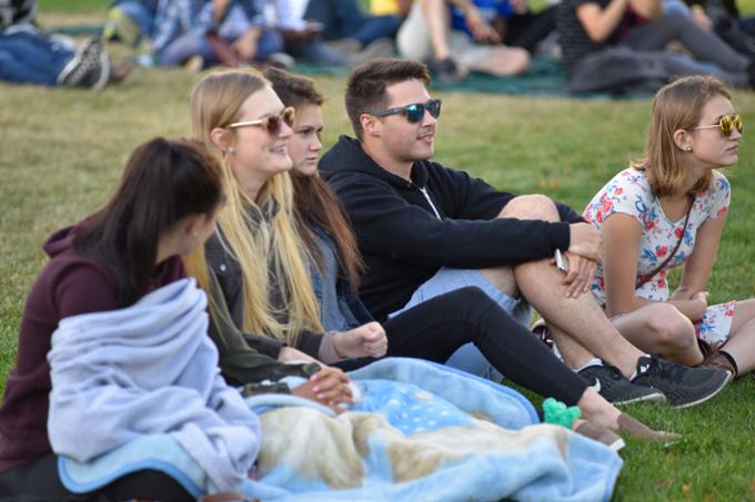 Five students watch a band while sitting on the academic green.