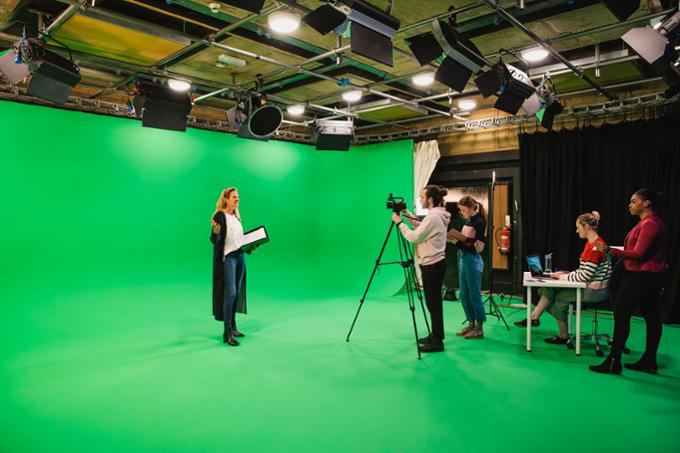 A film crew is recording a woman who is acting against a green screen.