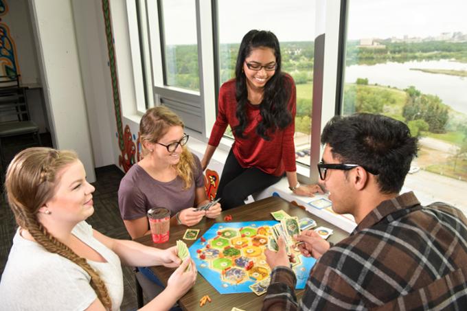 Four students plaing game at table in residence.