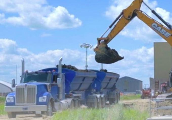 a backhoe moving sludge into a dump truck