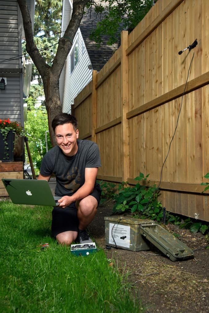 A student kneels in the grass while using a computer to conduct a test