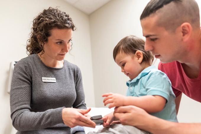A nurse practitioner helping a young father and a baby in a medical room.