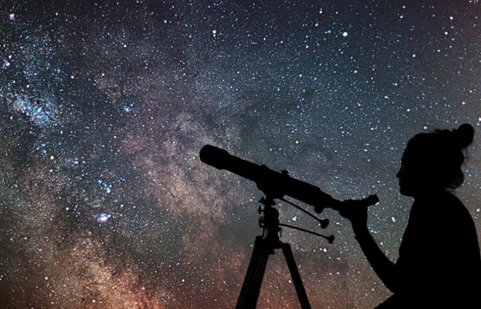 A scientist is using a telescope on a clear night with many stars