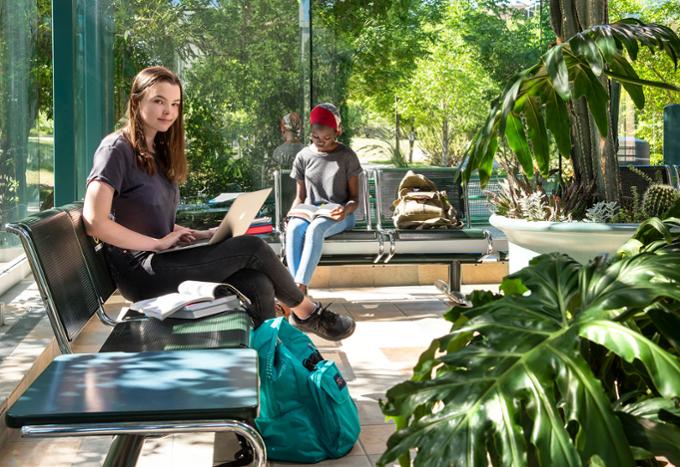 A student posing for a photo while another student studies in the background. They are both in the atrium on campus.