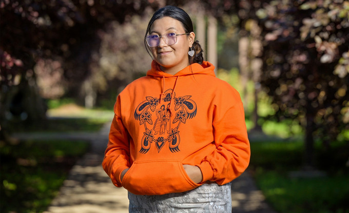 A person standing and smiling in an orange hoodie