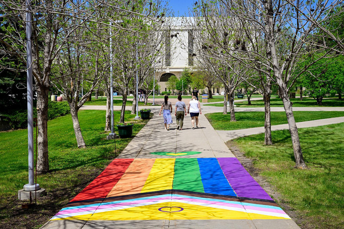 three people walking on a pride-painted sidewalk