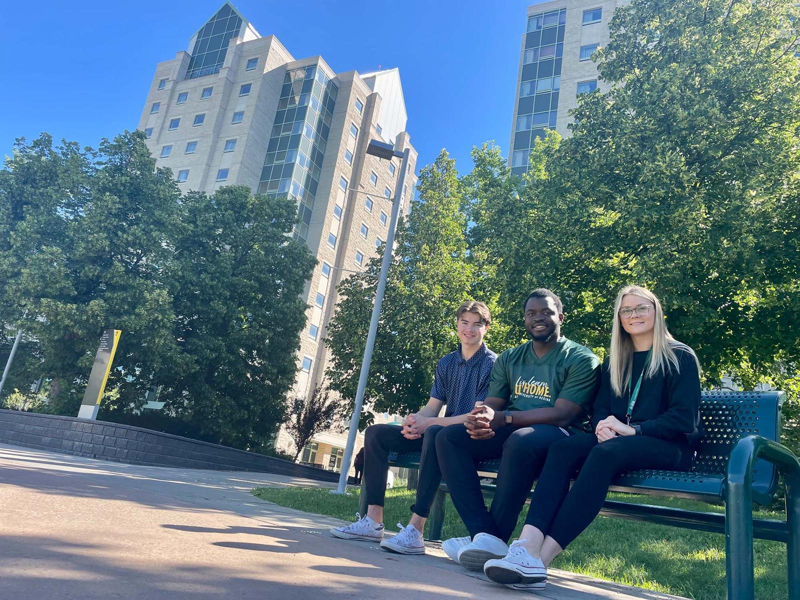 Three students sitting together on campus on a summer day.