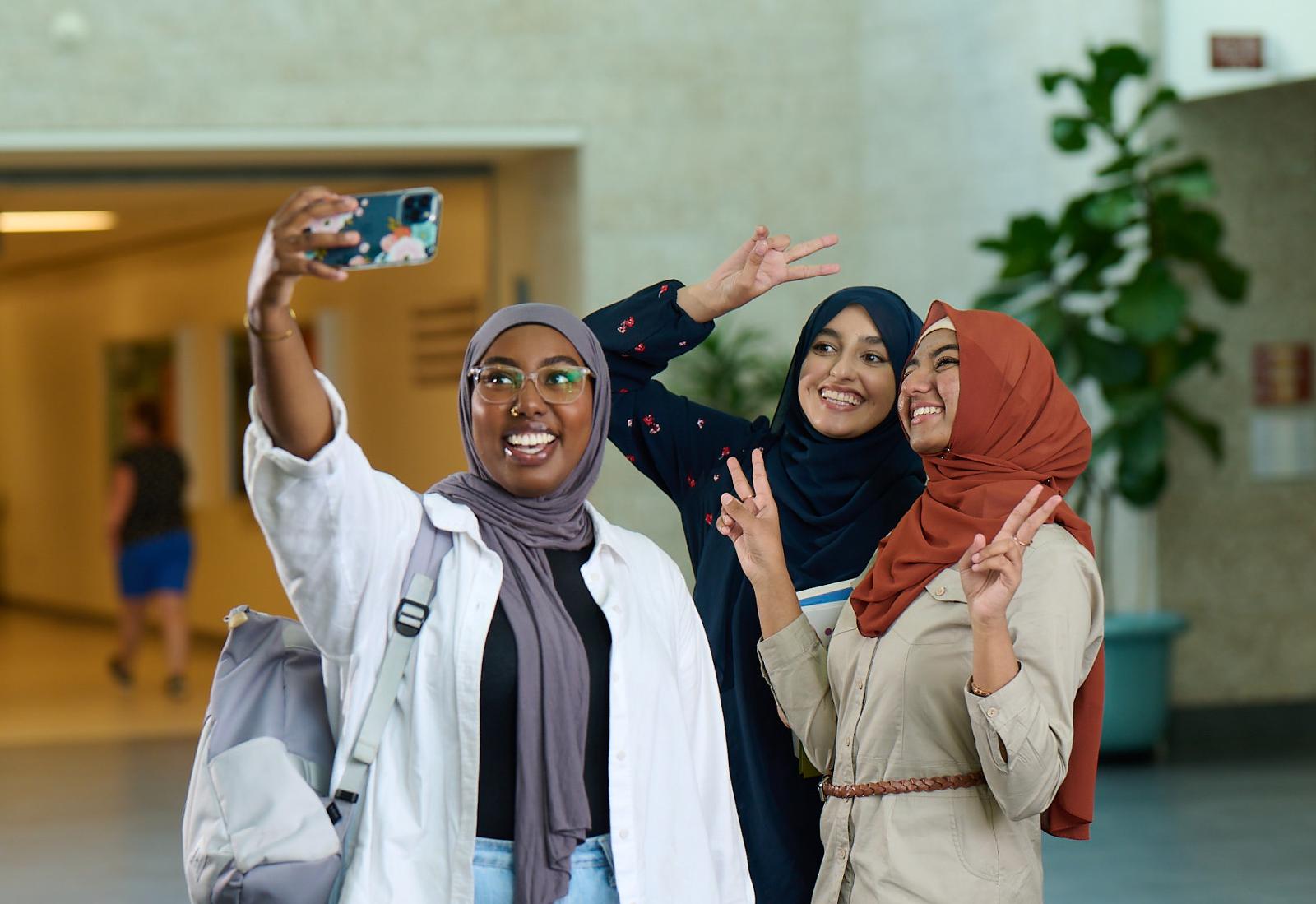 Three students taking selfies inside the University of Regina