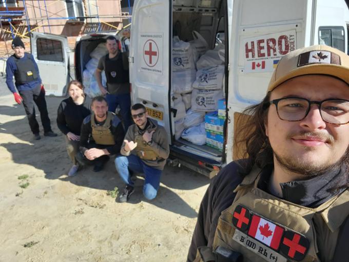 A man poses with his friends in front of a humanitarian vehicle in Ukraine.