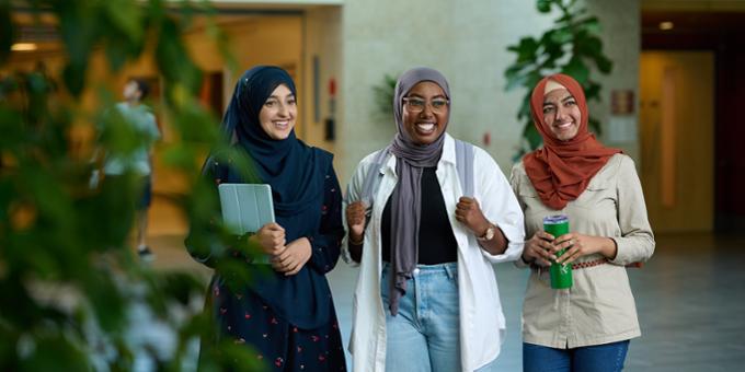 Three students walking through campus together, smiling and having a nice conversation.