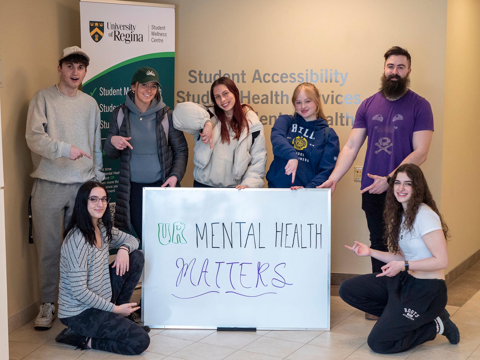 A group of students posing around a sign that says quote: Your Mental Health Matters, end quote