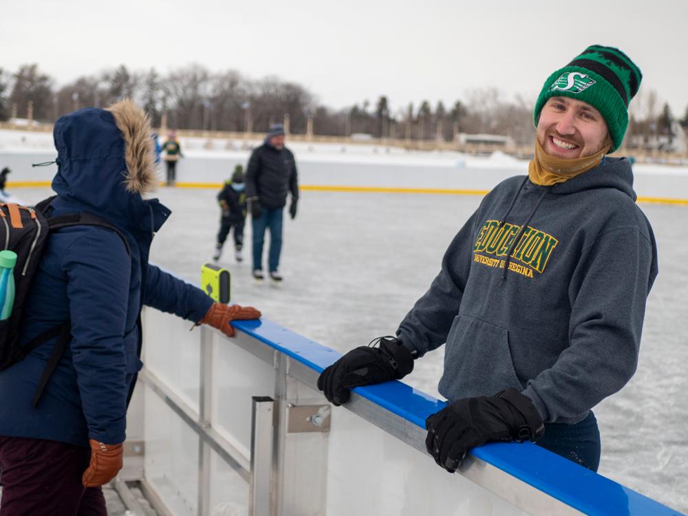 One smiling university student on skates at outdoor ice rink.
