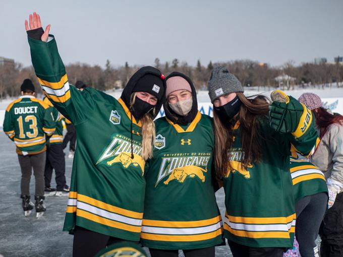 Three smiling university students on skates at outdoor ice rink.