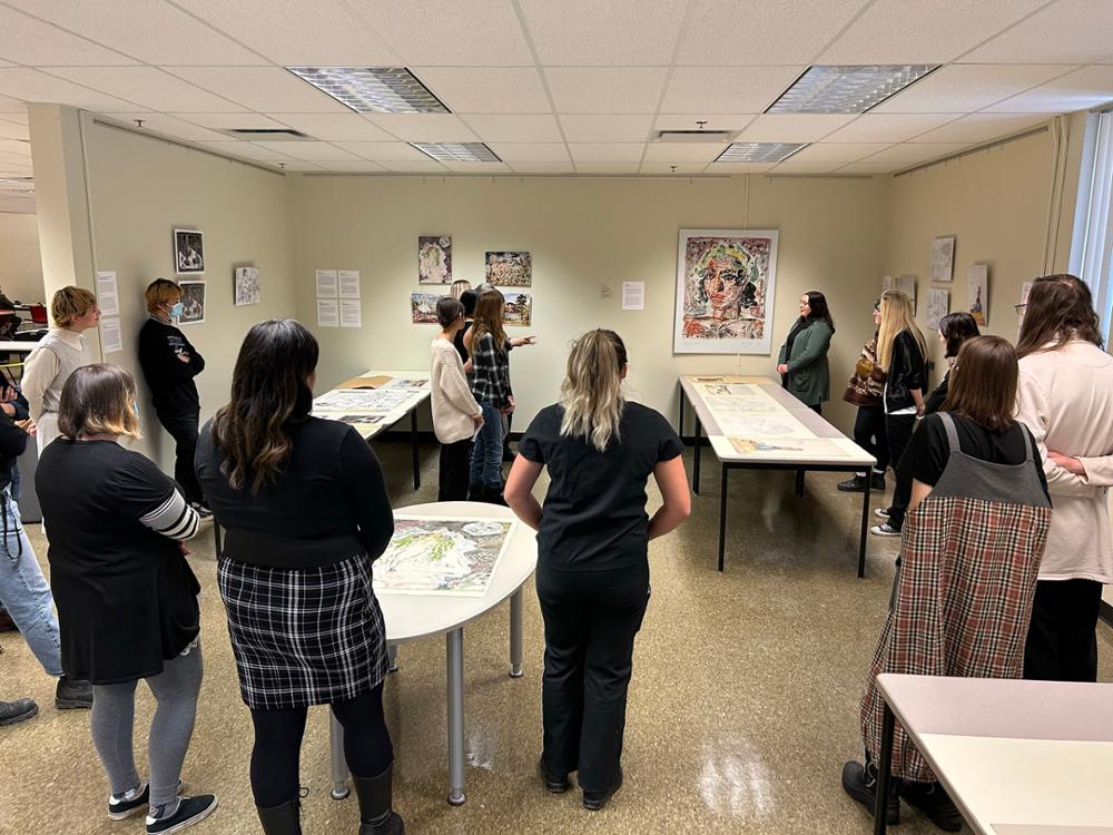 Students gather in a room with artwork displayed on the walls and tables.