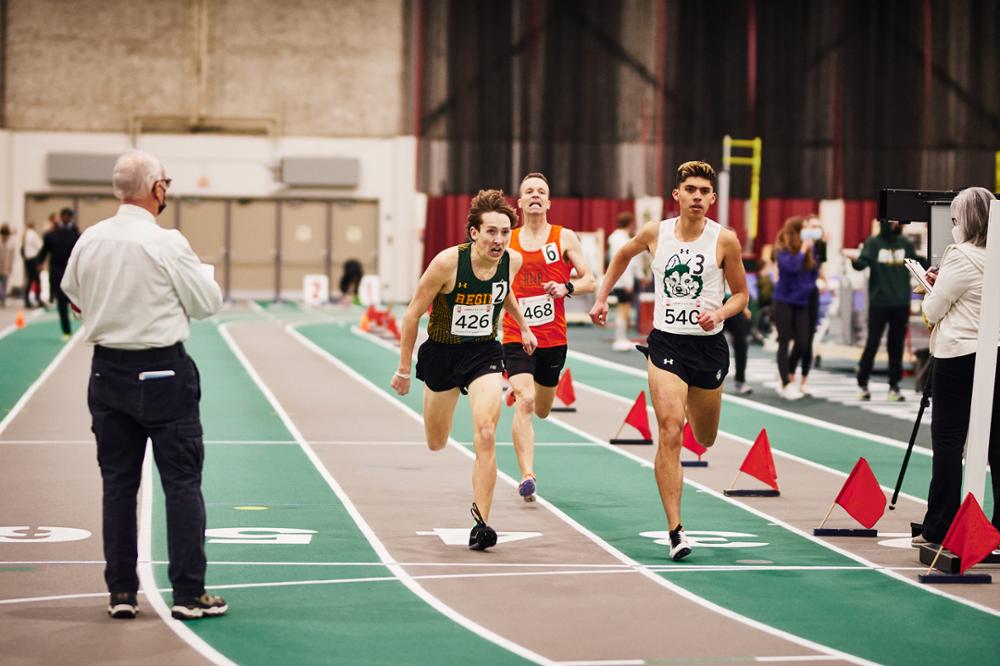 Three athletes running in a race on a track.
