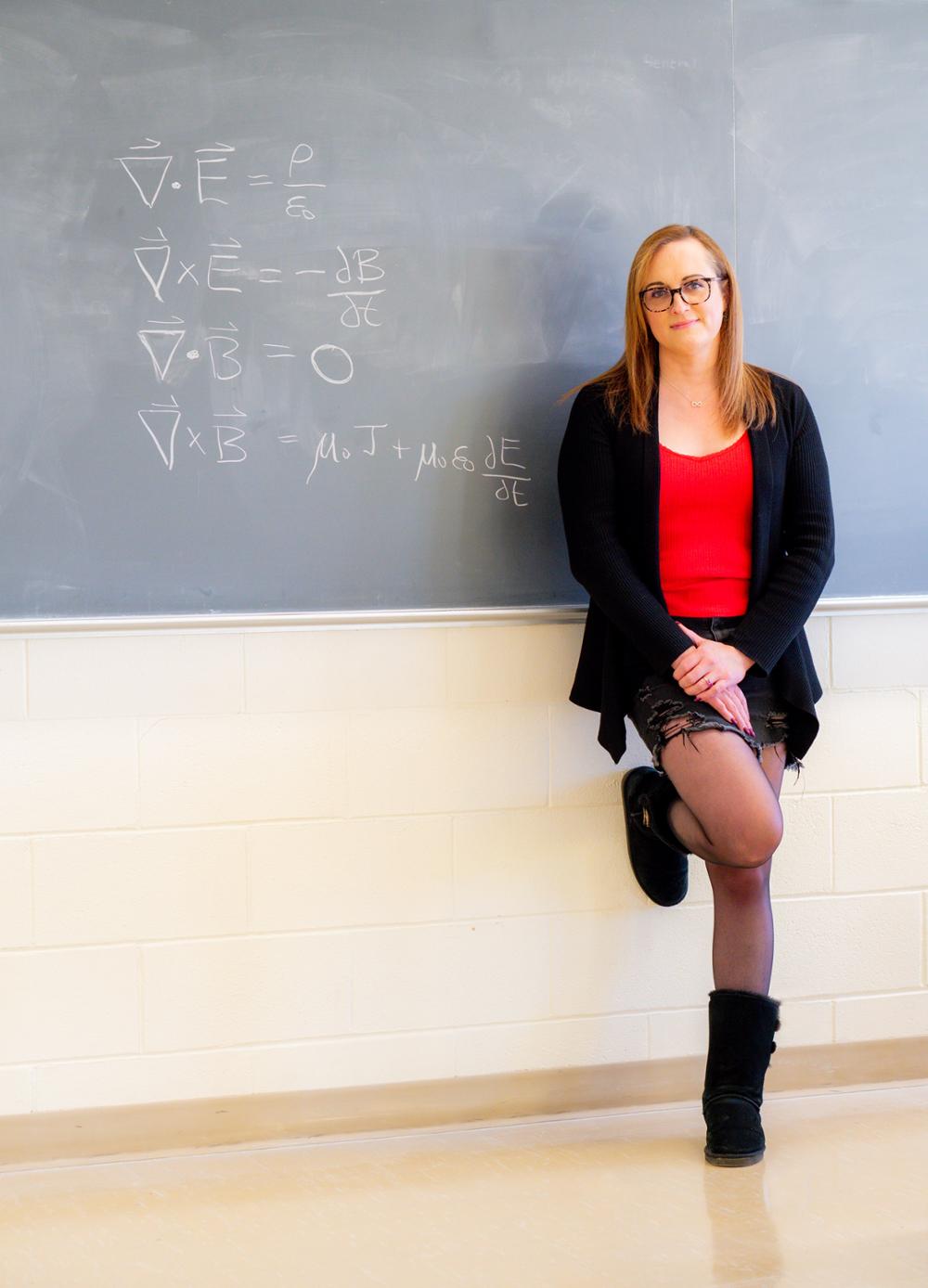 A professor standing in front of a blackboard with physics equations on it