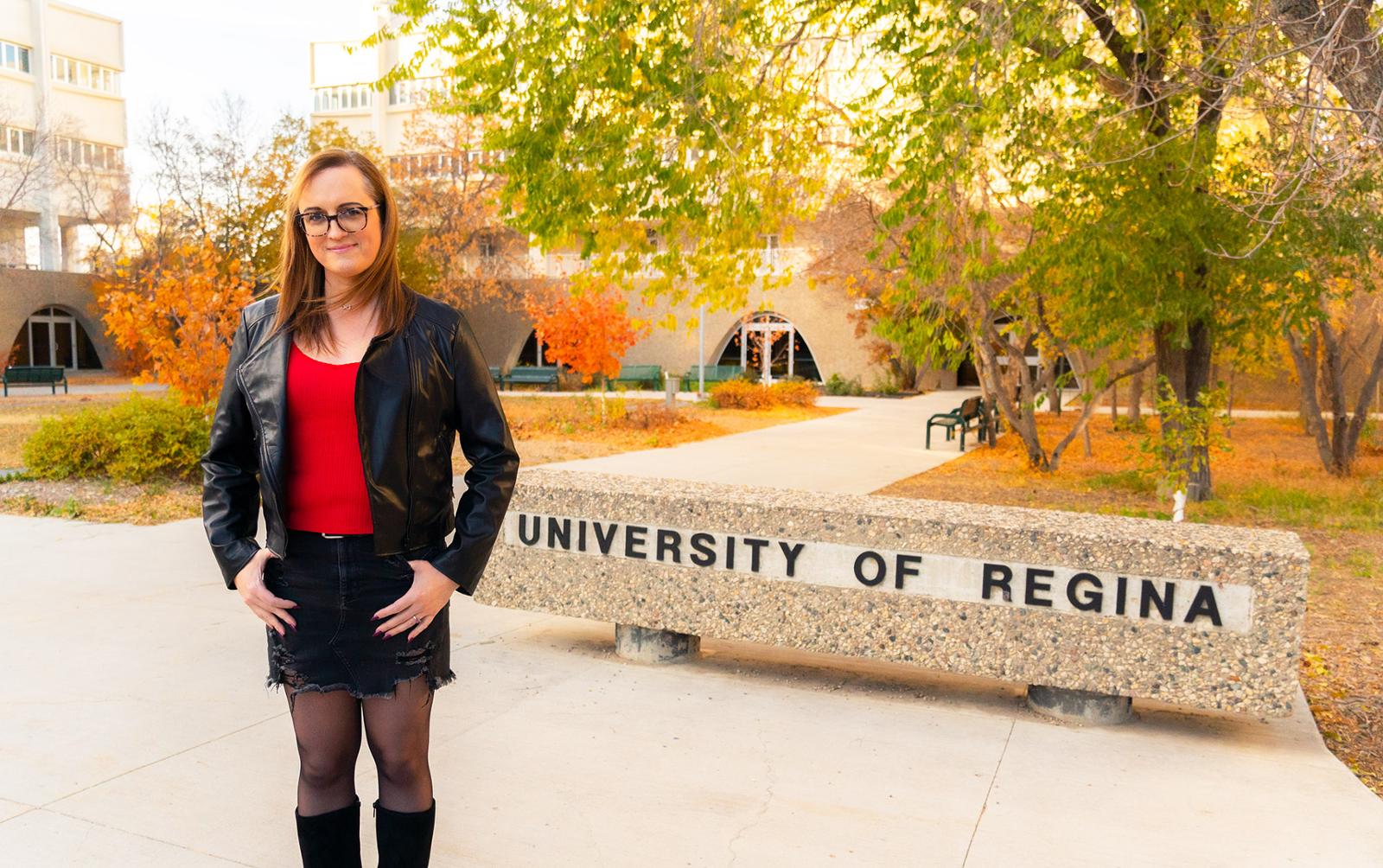 A professor stands in front of the secondary University of Regina sign on campus.