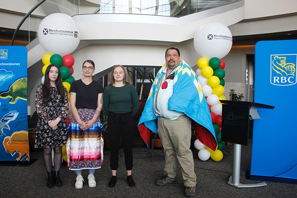 Four people pose in front of RBC banners and balloon displays. 