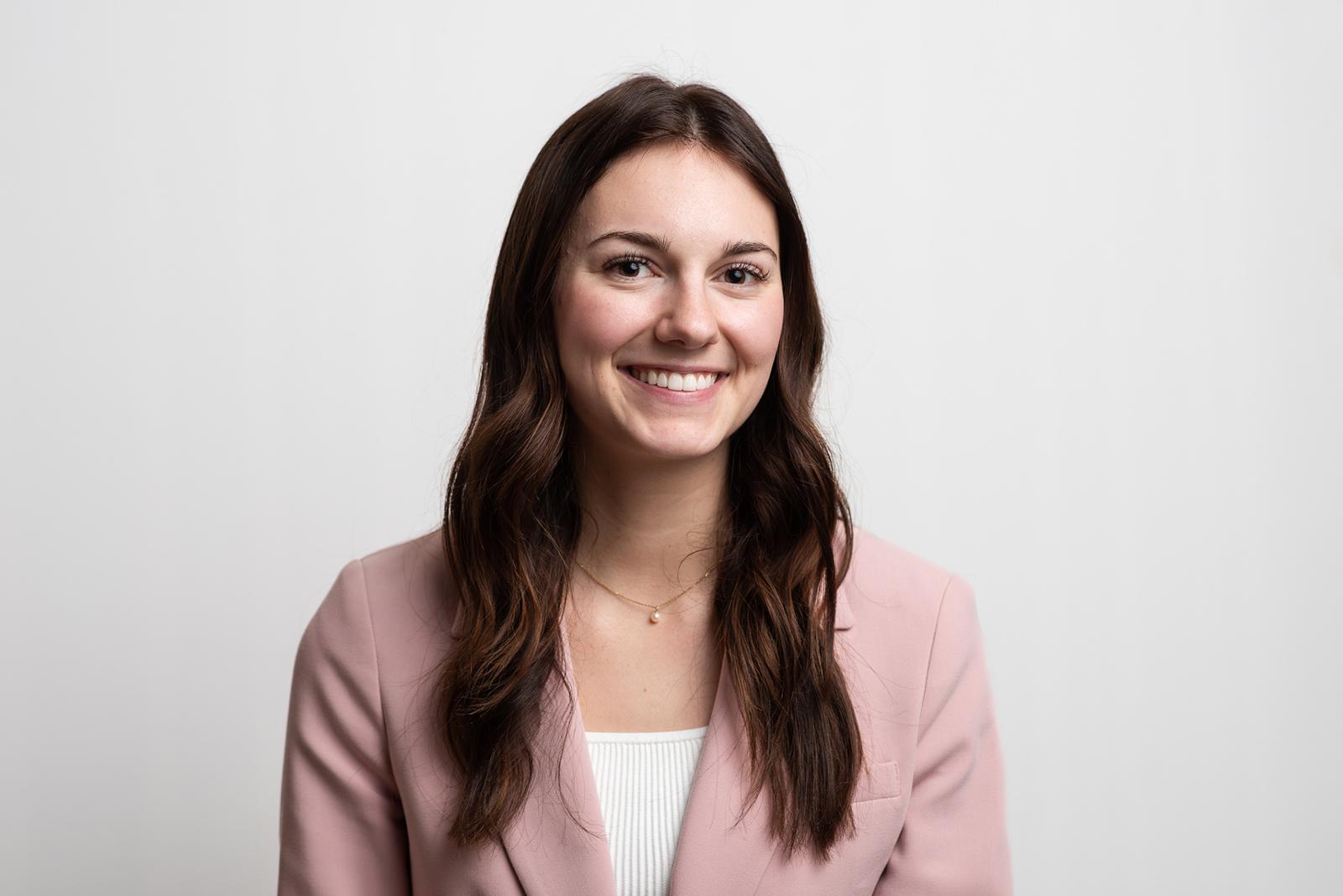 Isabella Grajczyk smiles for camera wearing a pink jacket over a white wool knit sweater.