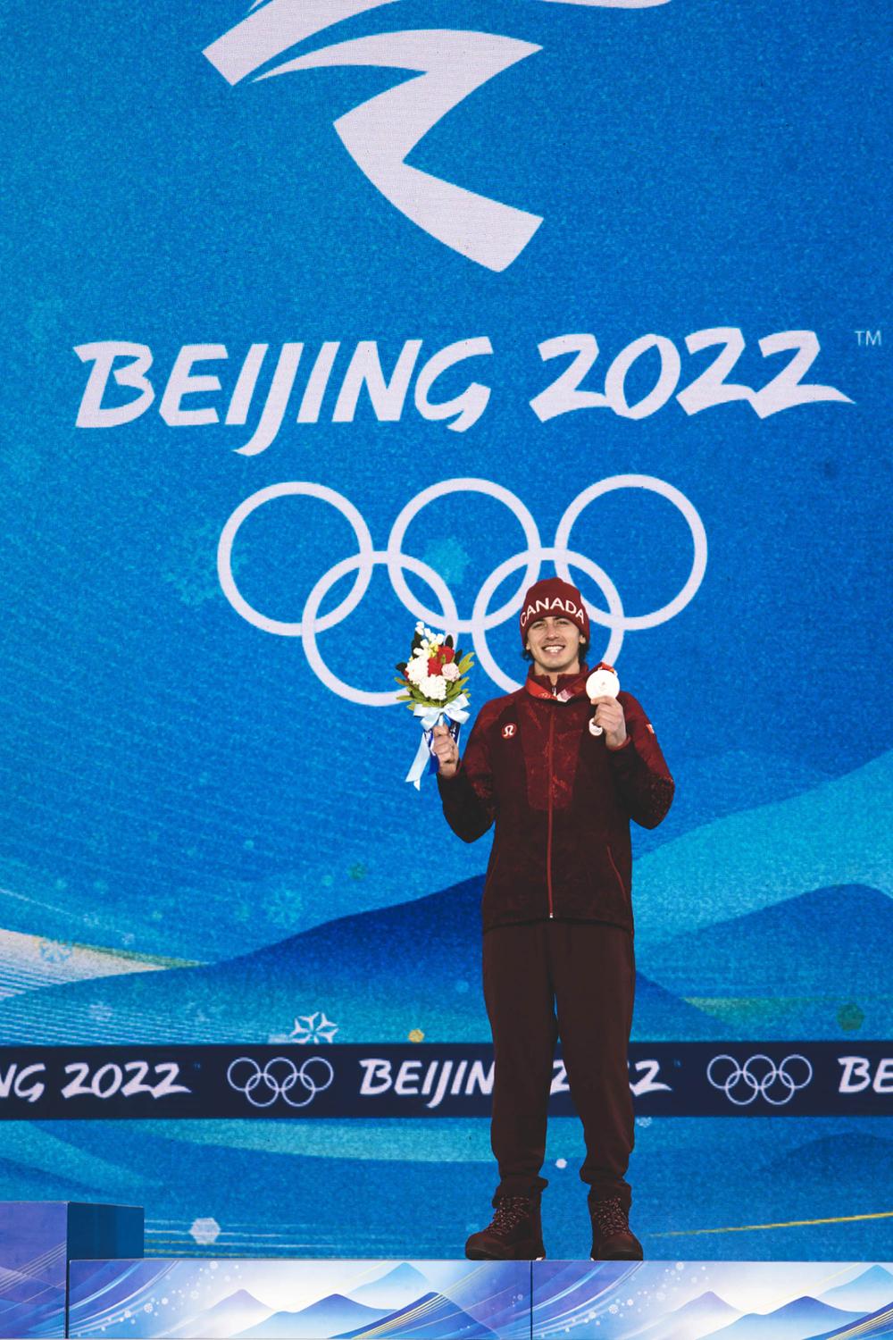 Mark McMorris on the Beijing Olympic podium holding his bronze medal and bouquet of flowers. 