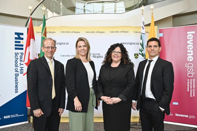 four people posing for a group photo in front of University of Regina banners and flags