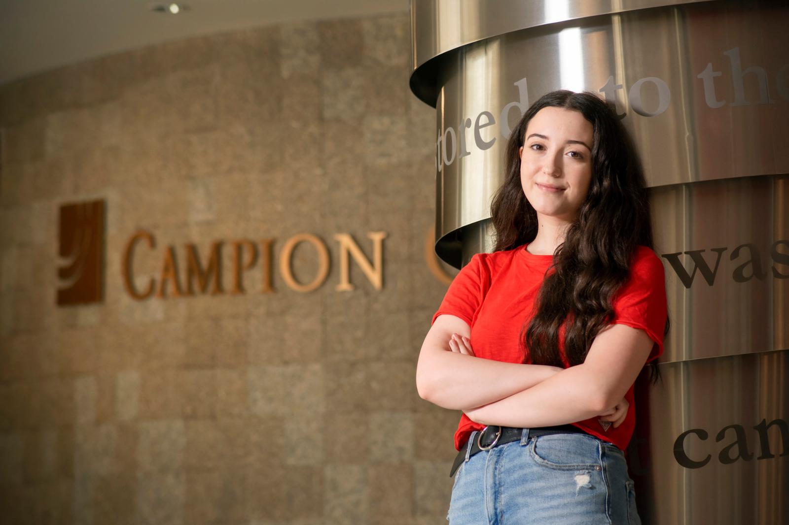 Student stands with arms crossed in front of wall that says Campion.