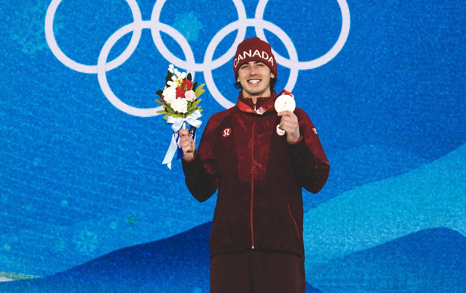 Mark McMorris on the Beijing Olympic podium holding his bronze medal and bouquet of flowers. 