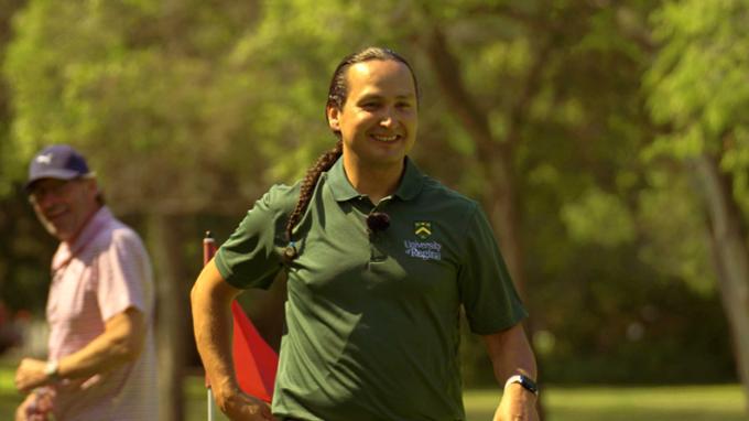 A man is walking down the fairway of a golf course.