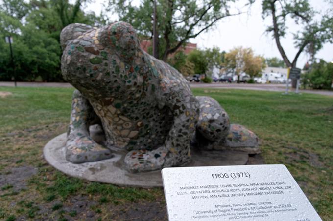 A large frog sculpture in a green park area.