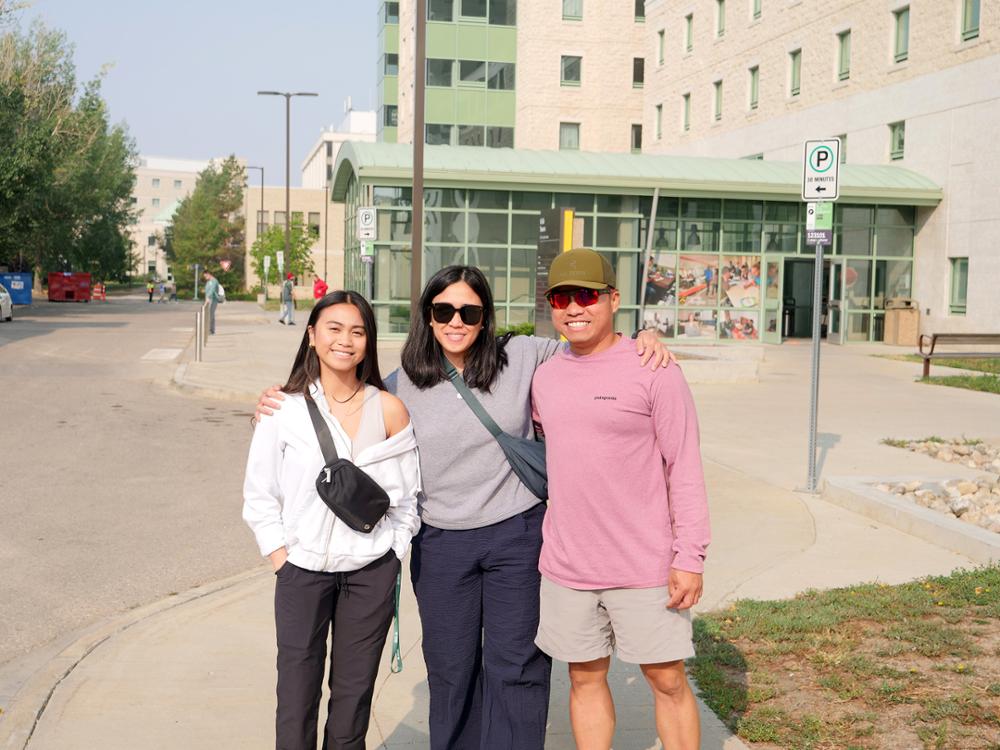 A family of three pose in front of residence.