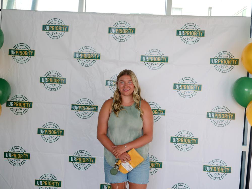 A single student poses in front of a U of R backdrop