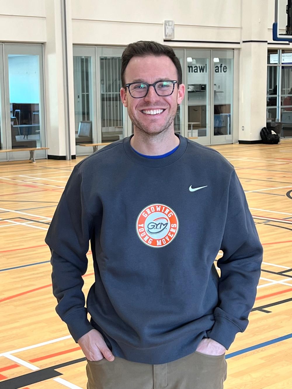 A smiling man wearing glasses and standing in a gymnasium