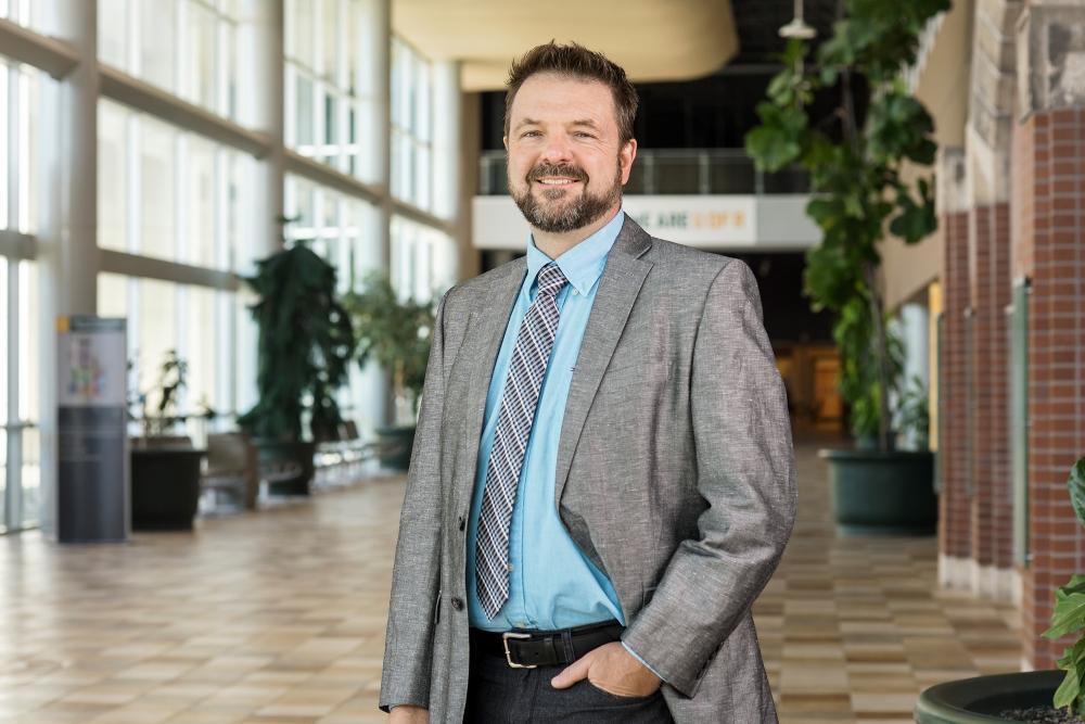 A smiling man wearing a suit and tie in a hallway