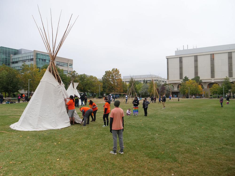 Various groups of people each working on several tipis at various stages of construction
