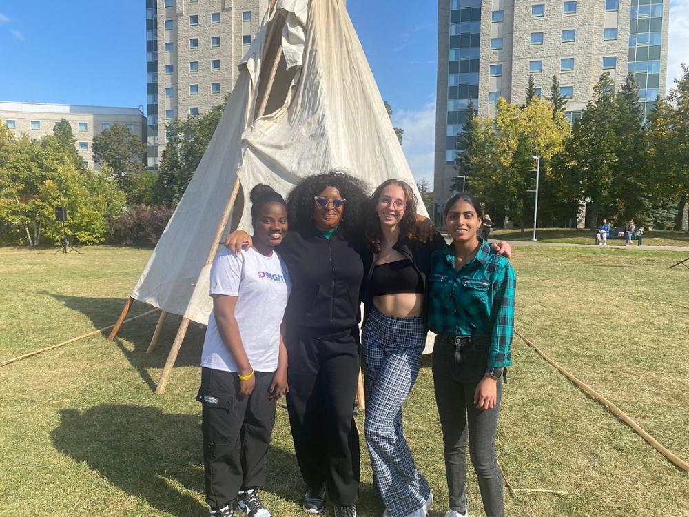 Four team members standing in front of an assembled tipi