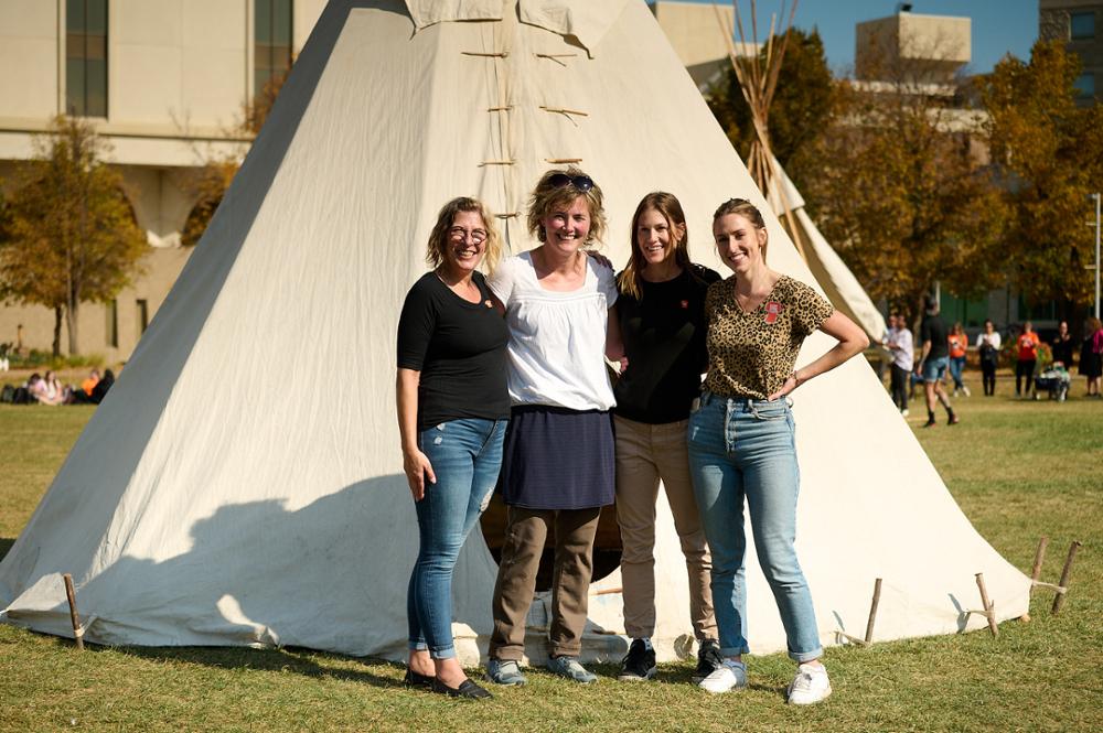 Four team members stand in front of an assembled tipi